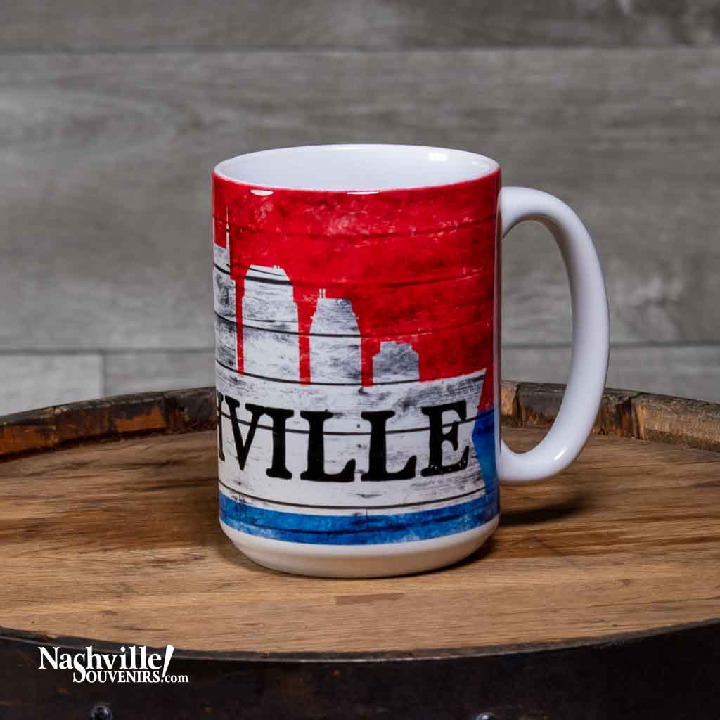 This "Nashville Skyline" Coffee Mug is a white ceramic mug with an easy to grip handle. The mug features a simple, yet attractive Nashville skyline design in red, white and blue. A big bold "Nashville" is printed in black.