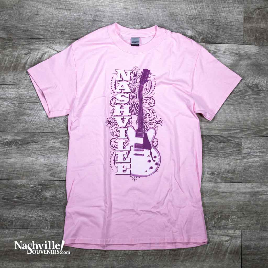 A pink Nashville Guitar t-shirts feature a large Nashville alongside an electric guitar. There is a nice filigree pattern in the background as well.