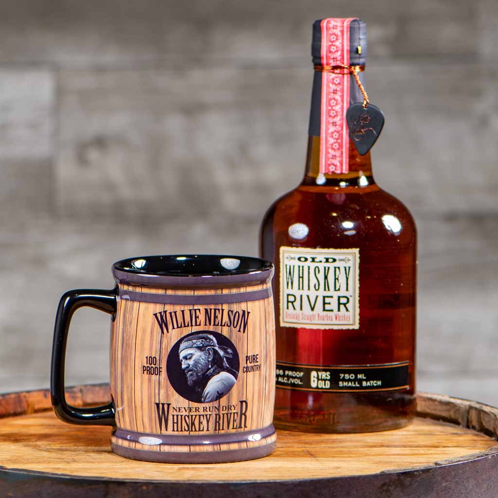 A Willie Nelson mug sitting beside an authentis bottle of Willie Nelson Whiskey River Whiskey.