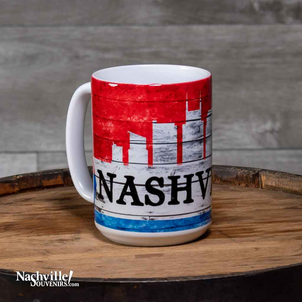This "Nashville Skyline" Coffee Mug is a white ceramic mug with an easy to grip handle. The mug features a simple, yet attractive Nashville skyline design in red, white and blue. A big bold "Nashville" is printed in black. 