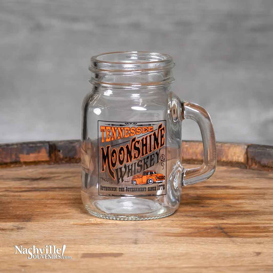 A new, oversized Tennessee "Moonshine Whiskey "Shot Glass printed with a rectangular logo featuring a moonshiners truck and "outrunnin' the government since 1779".