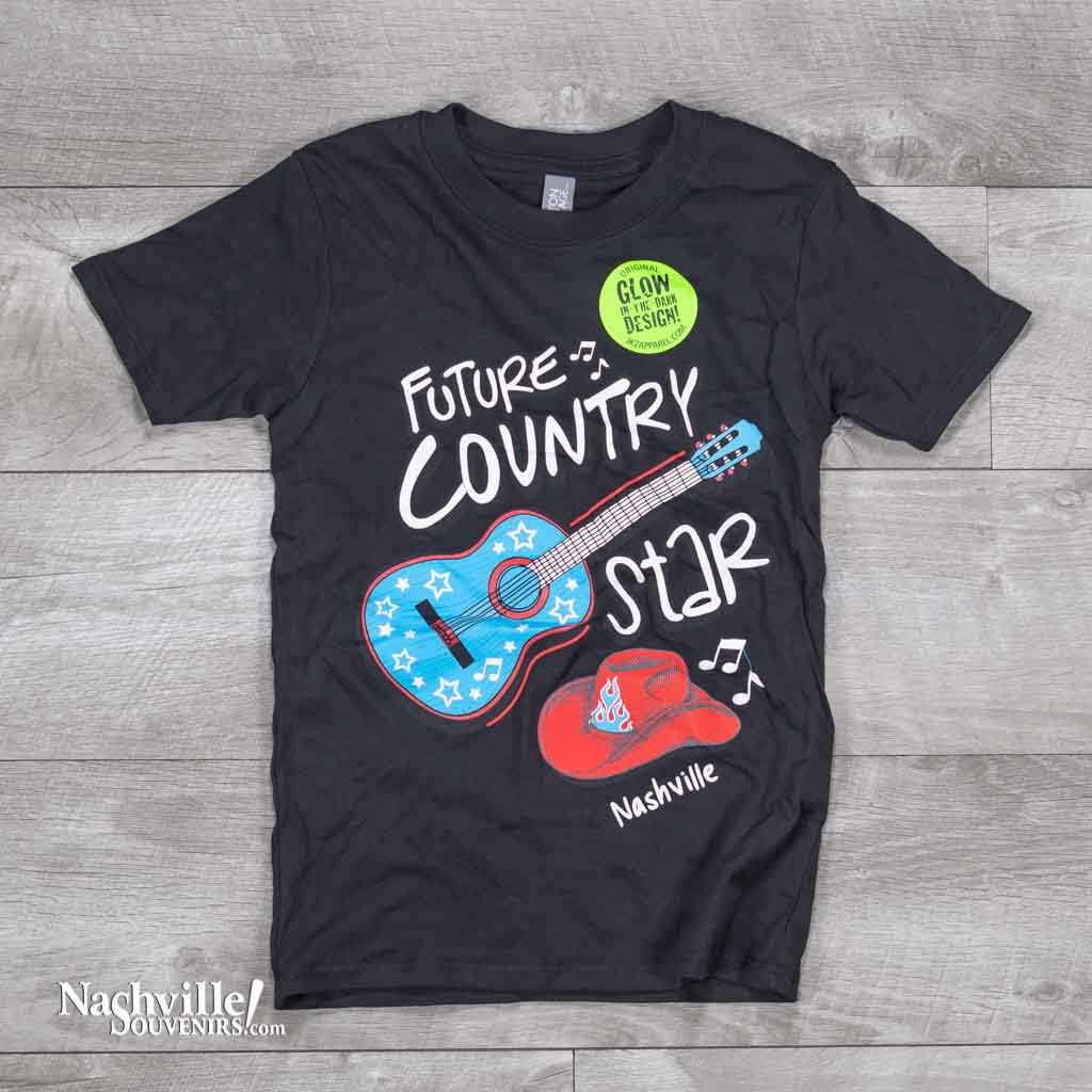 A great new glow in the dark design featuring a big bold blue and red guitar and Cowboy hat. Along with those images, printed in big letters are the words "Future Country Star Nashville" in black color.