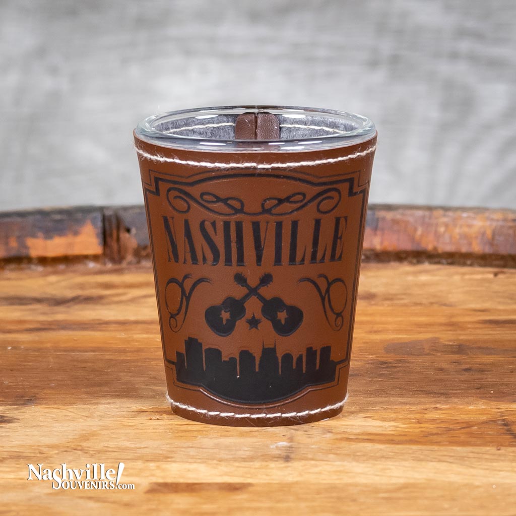 This Nashville Leathered and Stitched Shot Glass features a full wrap leather looking and stitched cover with embossed Nashville above a pair of crossed guitars.bold Nashville logo with guitar and the bottom glass reflects many different colors.